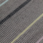 Detail of the Jasper Waffle Rug in Jet, widely spaced thin stripes of yellow, pink, black, acqua and white on a grey field. 