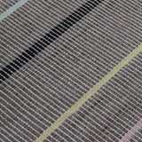 Detail of the Jasper Waffle Rug in Jet, widely spaced thin stripes of yellow, pink, black, acqua and white on a grey field. 