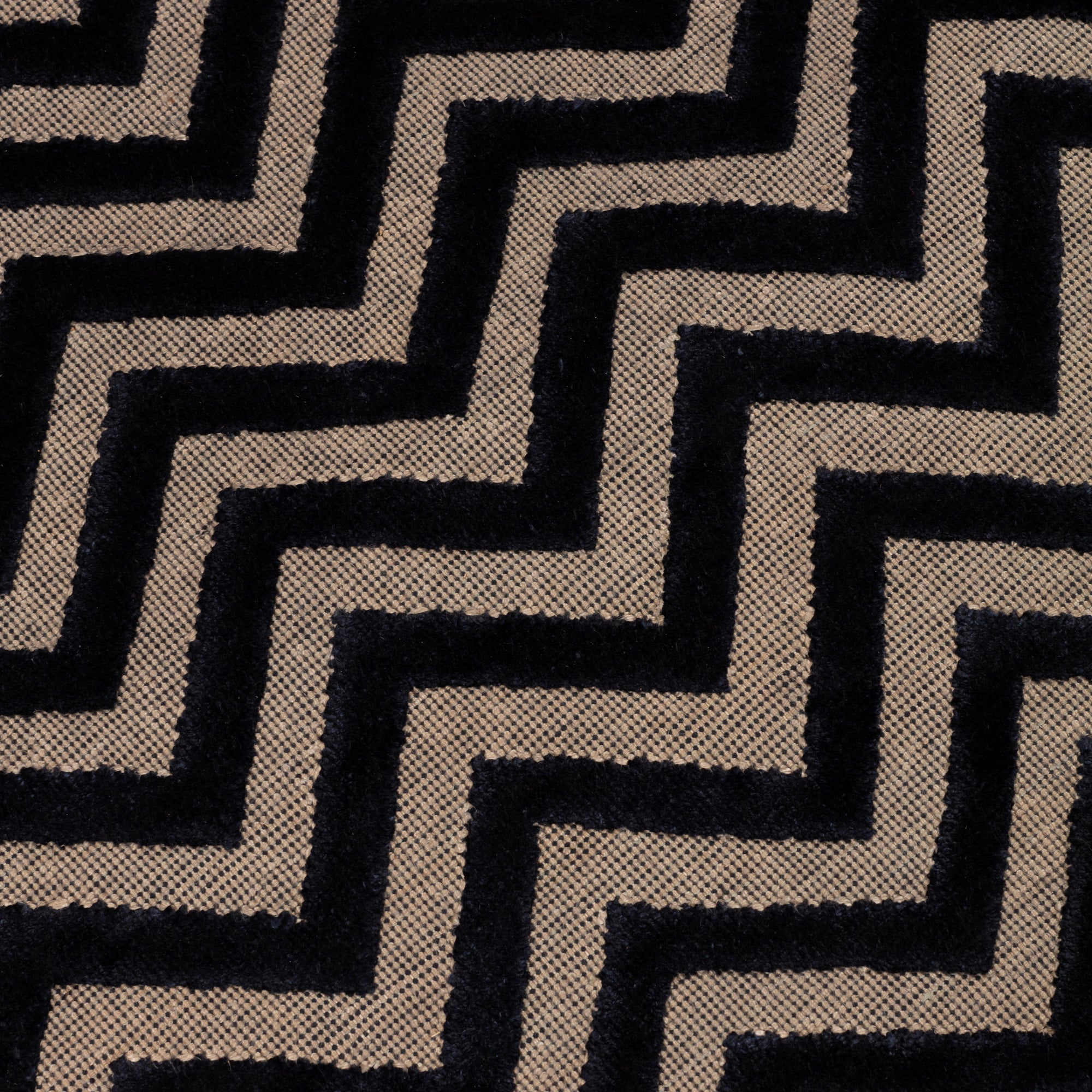 Detail of the Penta Chevron Rug in Jet, a black chevron pattern on a taupe field with a wide solid border. 