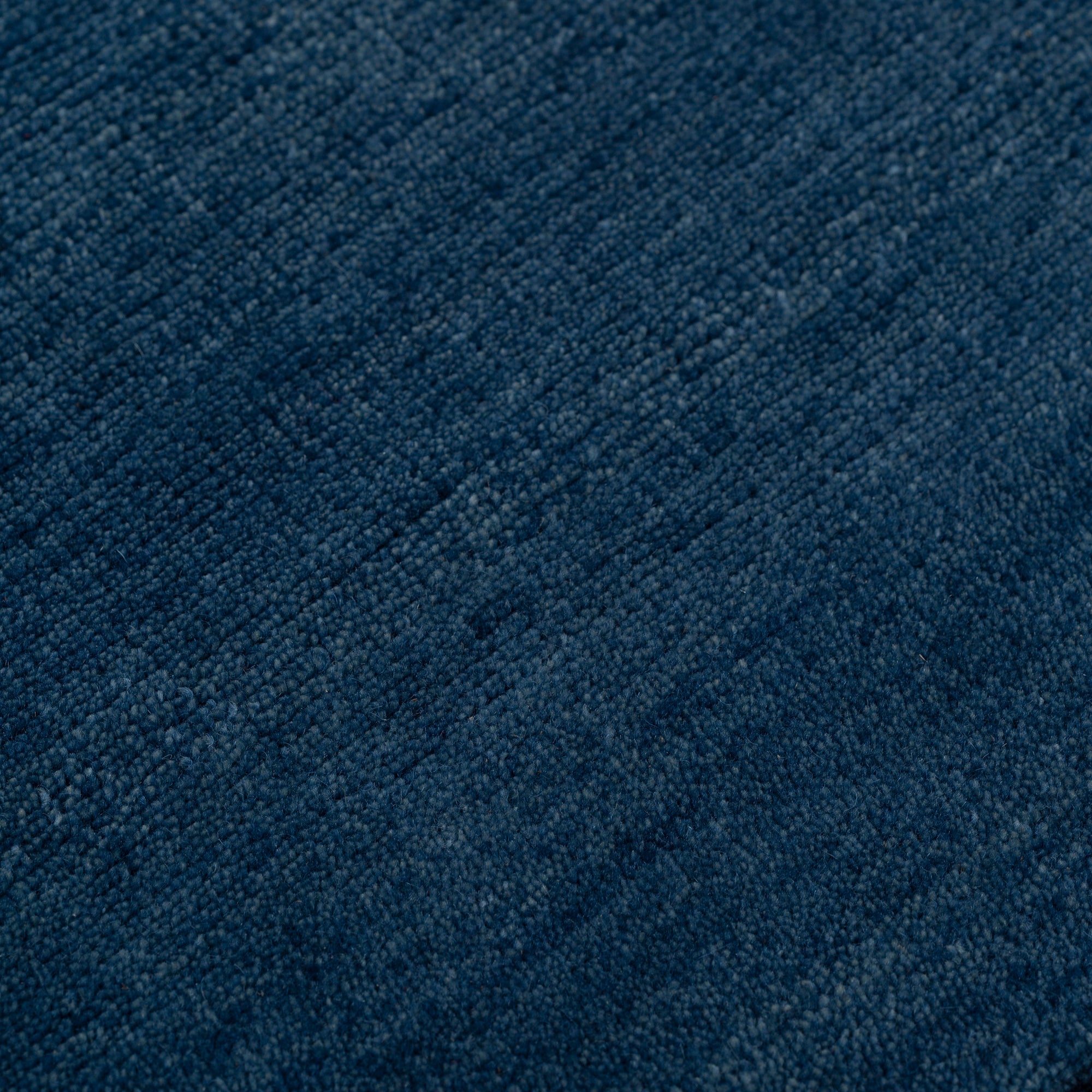 Detail of the Plain Stitched Border Rug in Prussian Blue, a solid indigo rug with a black border with black border with blue and taupe dashes. 