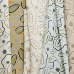 A row of fabric swatches, all in the same large-scale minimal floral print in different colorways with tan, cream and white fields.