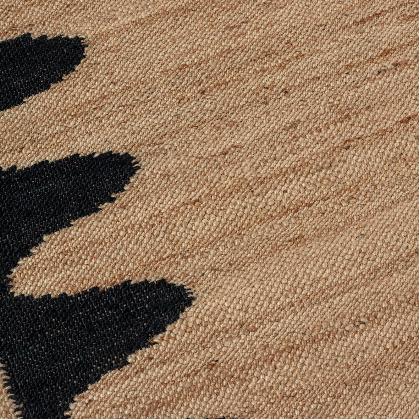 Detail of the Waver Rug in Jet Black, a strated ecru field with a black flame stitch border. 