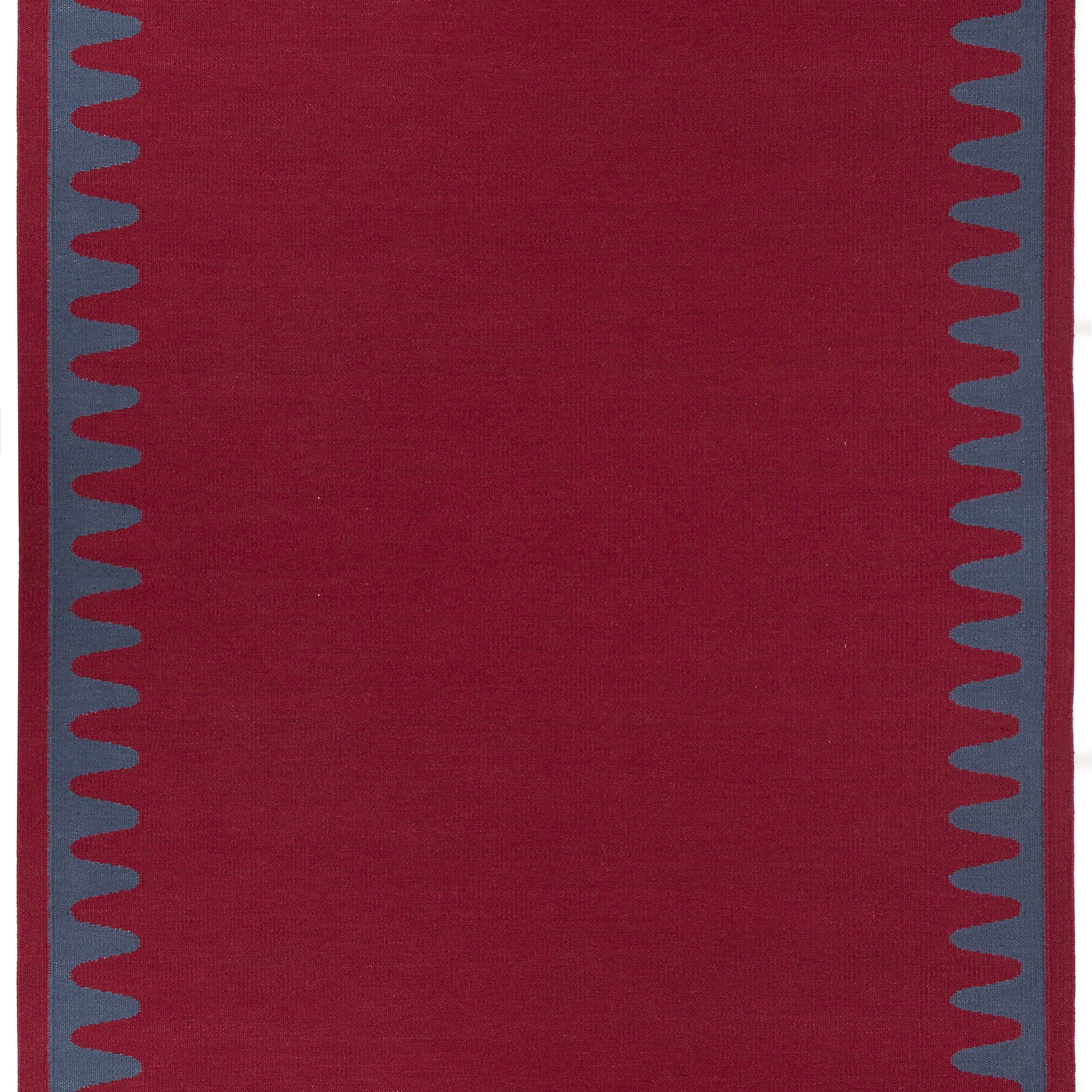 Waver Rug in Queensdown Red, a solid red field with a blue flame stitch border. 