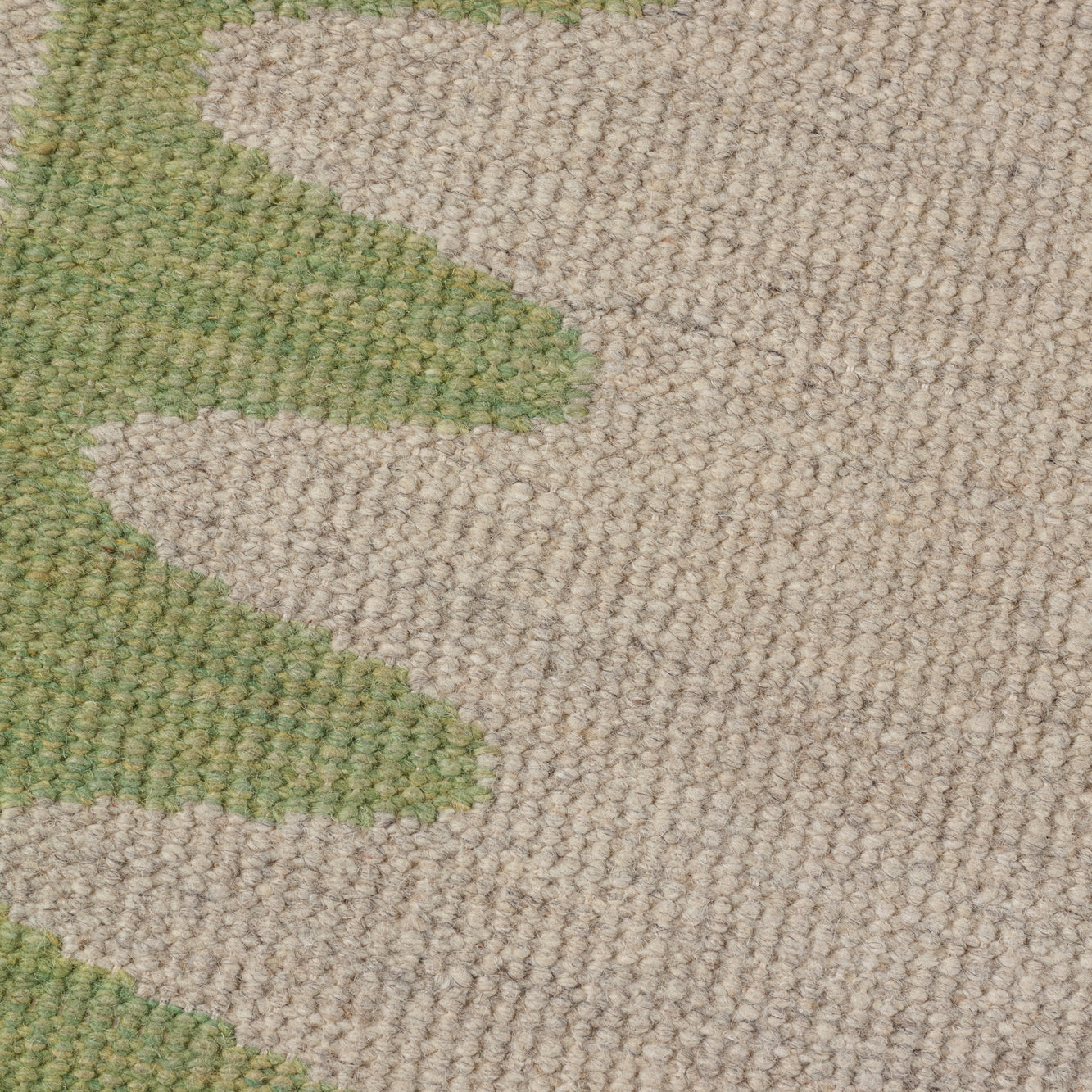Detail of the Waver Rug in Sage, a strated taupe field with a sage green flame stitch border. 