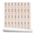 A hanging roll of wallpaper with repeating rows of a watercolor flowers in tan and gray on a light pink background.